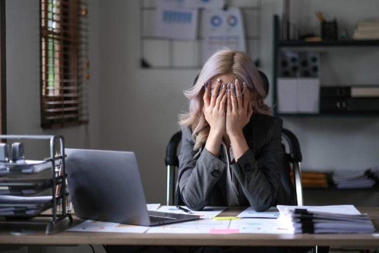 woman with anxiety at work desk face in hands