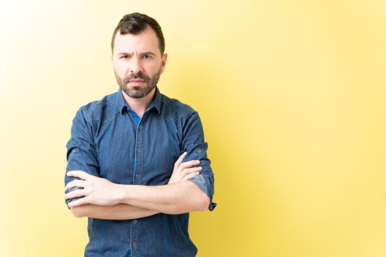 man in denim shirt with arms crossed angry